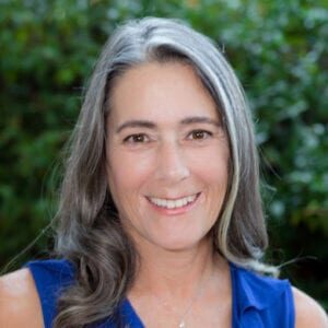 A woman with long grey hair wearing blue shirt.